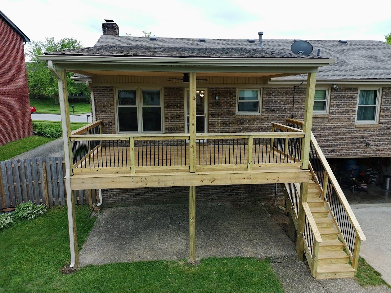 Raised wooden deck with railing and stairs attached to a stone house in a backyard