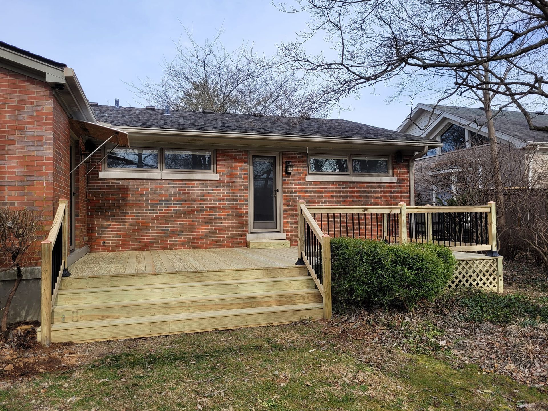 Brick house with small front porch, wooden steps, and a fenced yard under bare trees