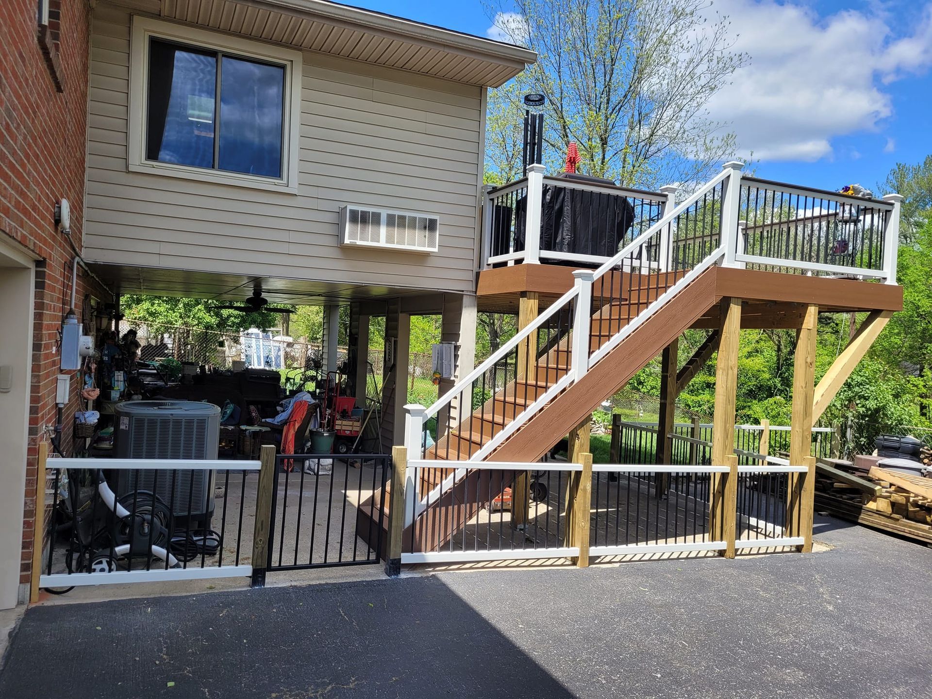 Raised wooden deck with white railing and stairs beside a brick house over a paved driveway