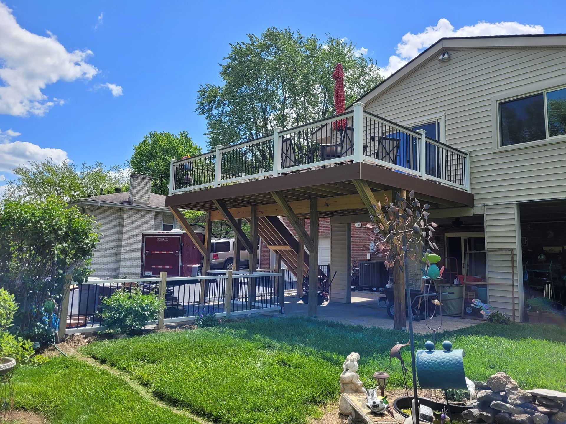 Backyard deck with stairs, patio furniture, and green lawn beside a house on a sunny day