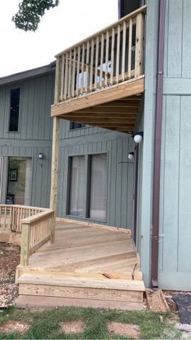 Exterior wooden balcony and deck on a gray apartment building, with stairs and railings.