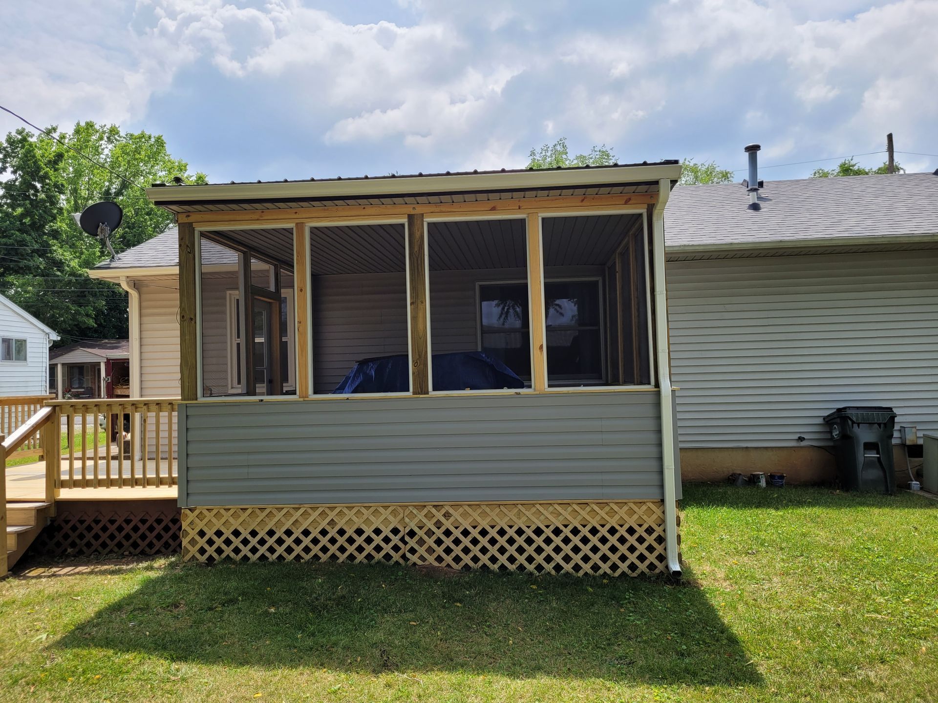 Back porch sunroom with screened windows, tan siding, and lattice skirting on a grassy yard