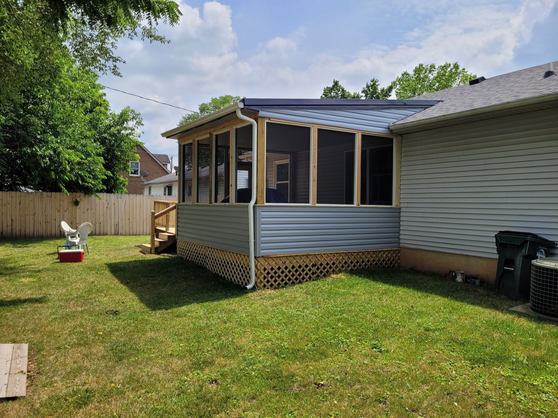 Screened porch attached to a white house, with a grassy backyard and a small yard decoration.