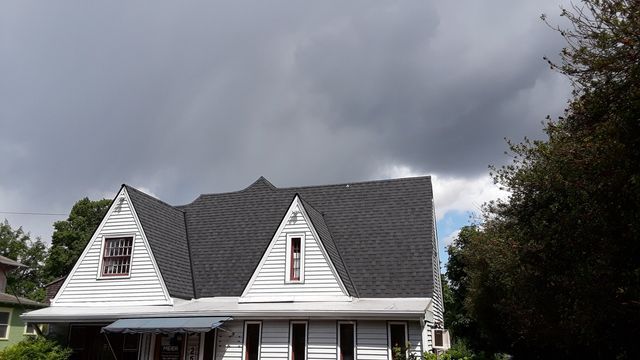 a white house with a gray roof and a cloudy sky in the background