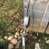 A chainsaw is sitting in the grass next to a brick wall.