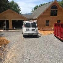 A white van is parked in front of a wooden house under construction.