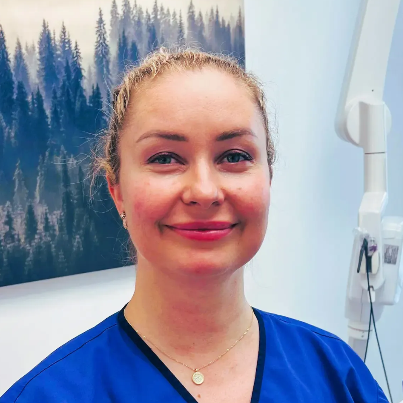 Tannlege Christian med briller og skjegg, iført blå skjorte og medisinsk maske, smiler til kameraet.