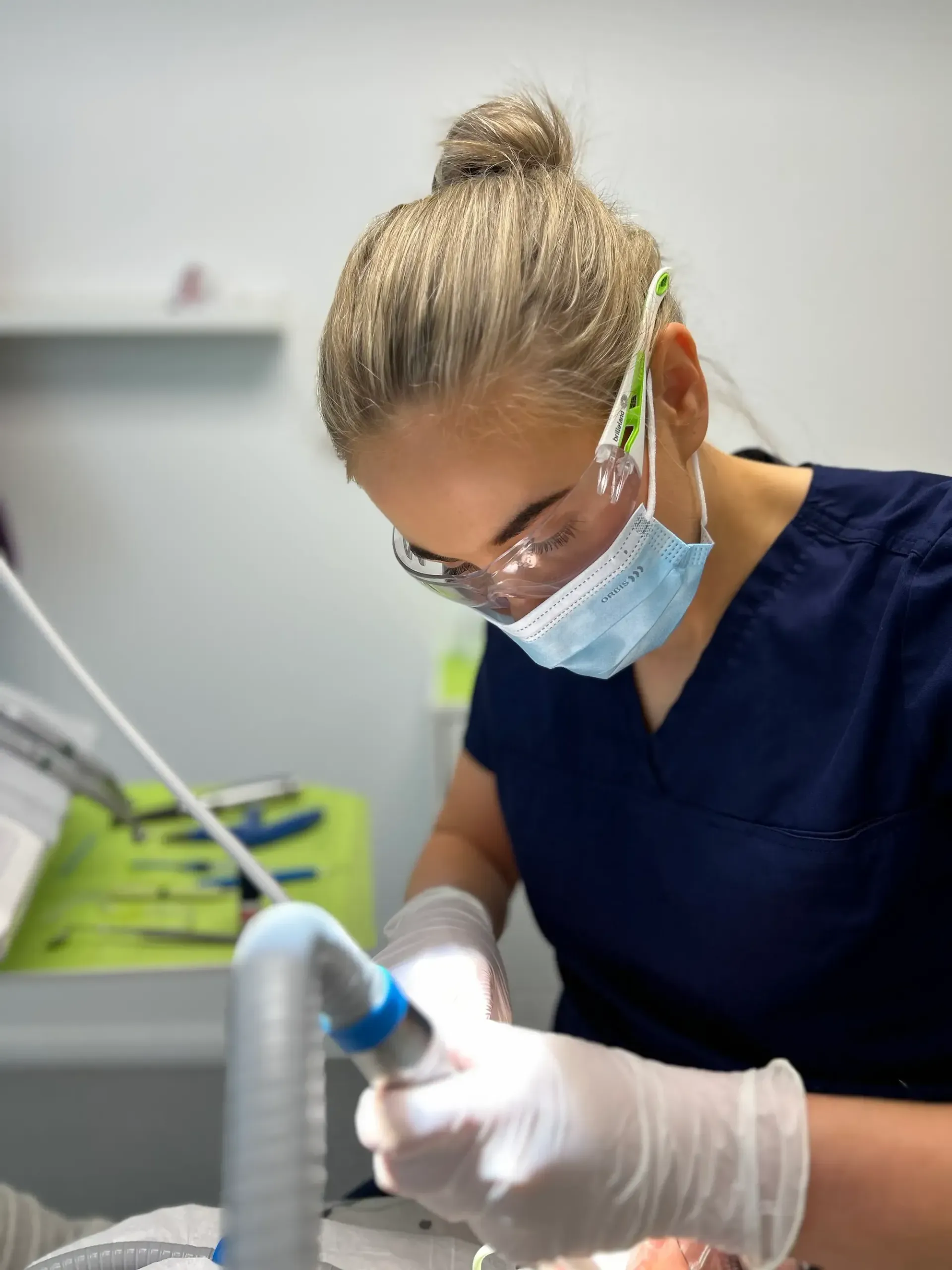 Seks kvinner i skrubber smiler i lyse omgivelser innendørs.