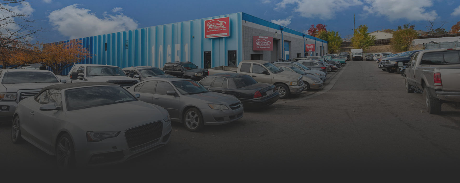 Car dealership lot with rows of parked cars in front of a blue-and-white showroom. | Accurate Automotive Northglenn