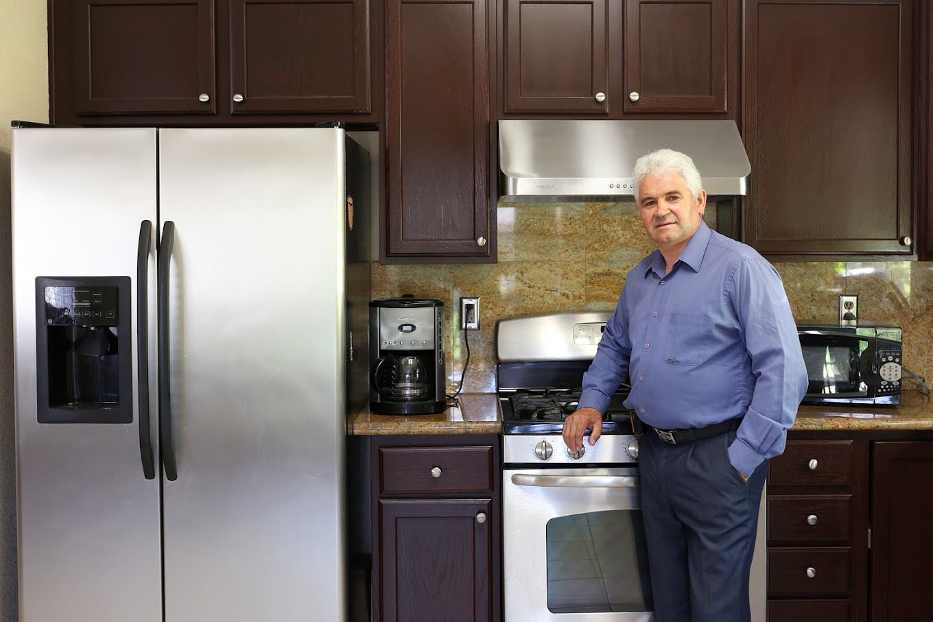 a man is standing in a kitchen next to a refrigerator and stove . Fresno appliance repair