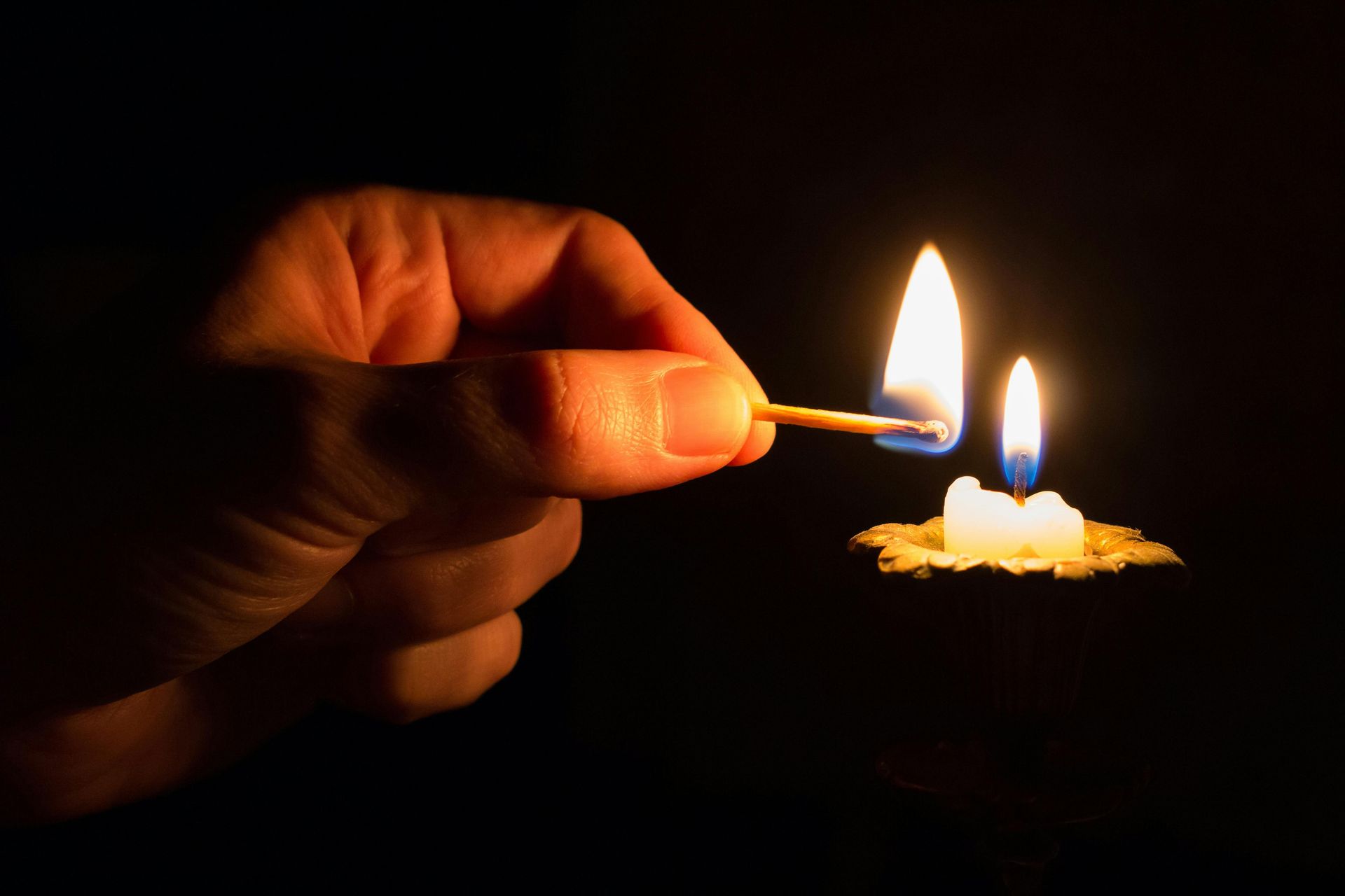 Hand holding a lit match, igniting a candle in the dark.