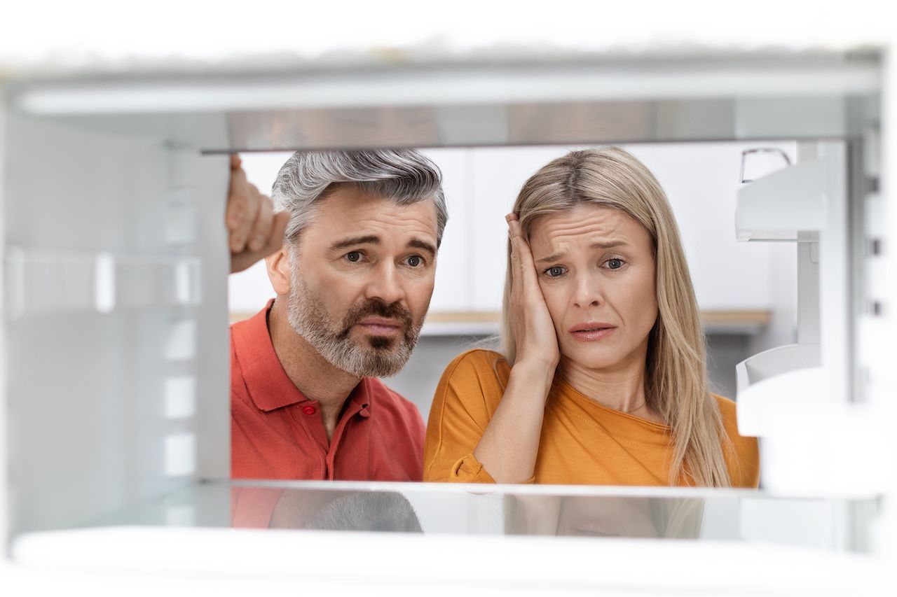 a man and a woman are looking into an open refrigerator .