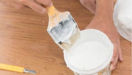 Painter dipping his yellow paintbrush into a small can of white paint.