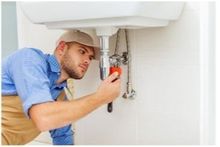 Handyman completing various plumbing services and repairs wearing a blue shirt and grey hat.