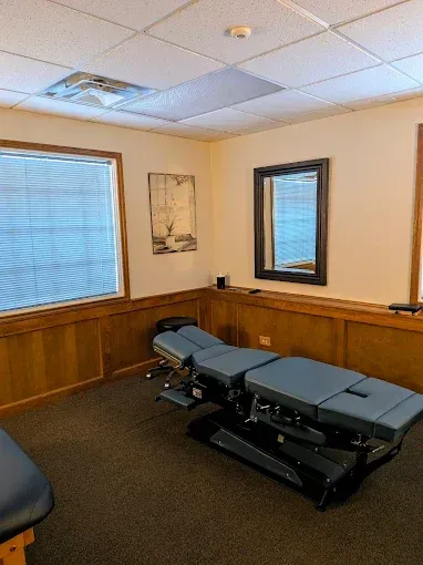 Chiropractor's office: Treatment table, dark walls, window with blinds, mirror, and artwork.