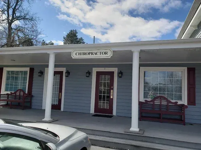 Chiropractor's office with blue siding, red doors and window trim, white columns, and a sign.
