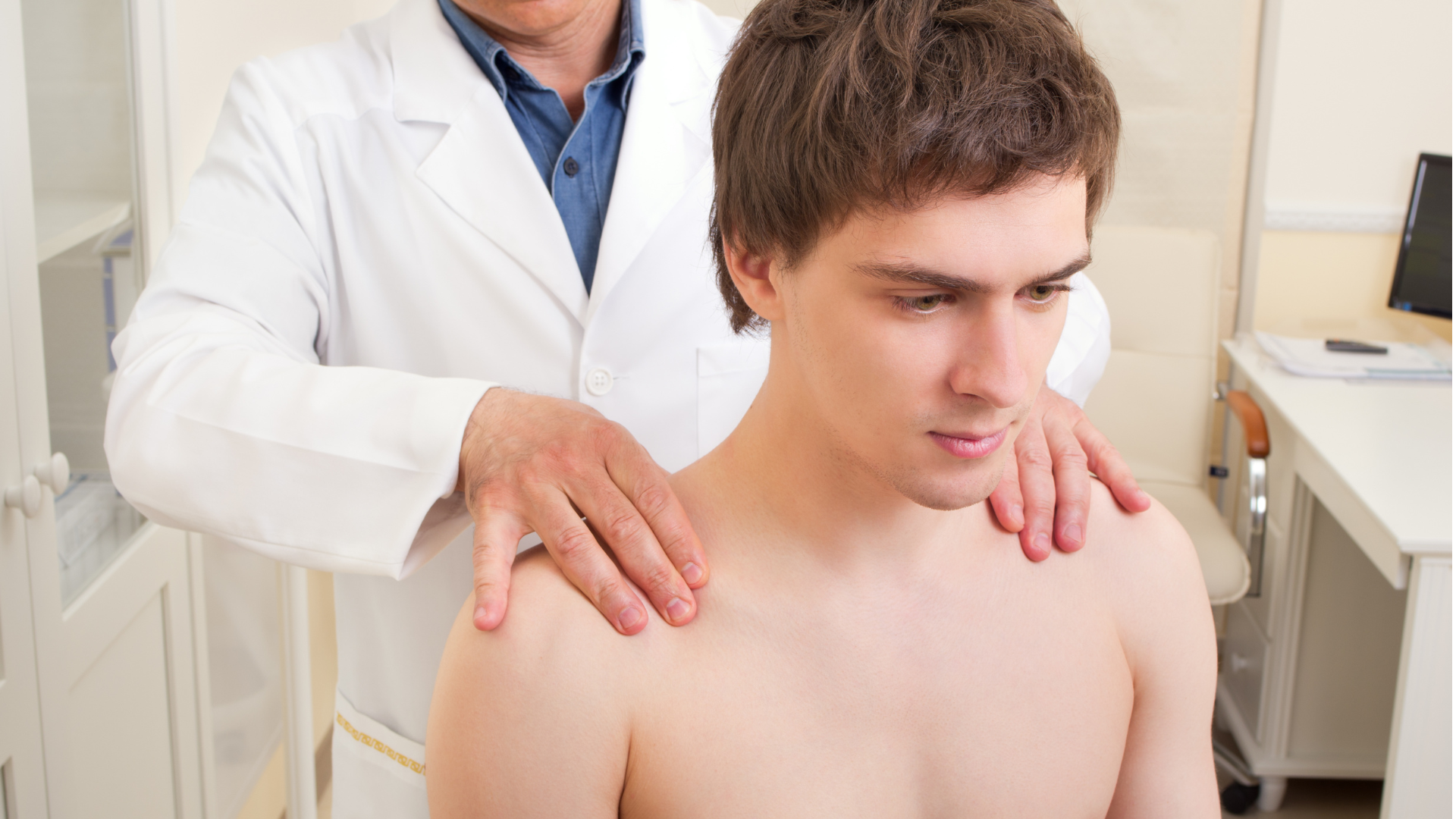 Doctor examining a shirtless person's shoulders in an office setting.