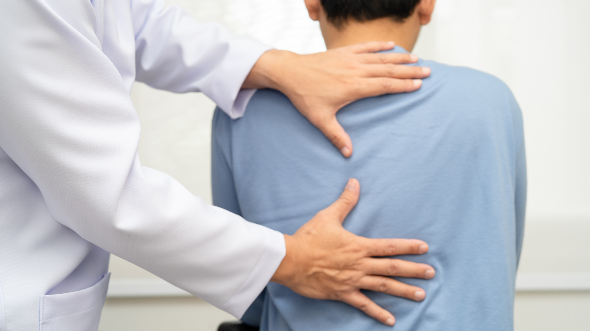 Doctor examining a patient's back. Hands on back; both wearing light colors.