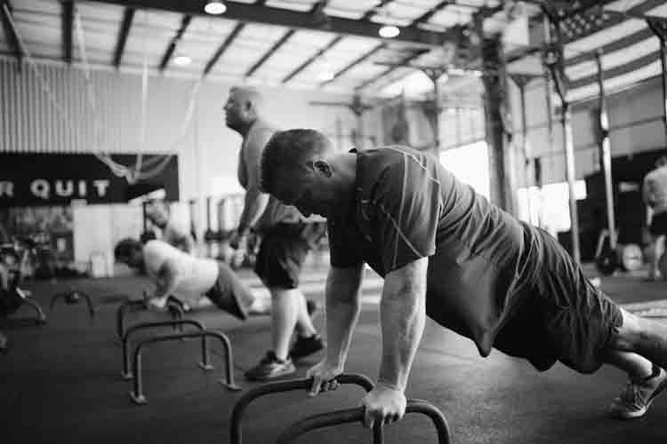 A group of men are doing push ups on bars in a gym.