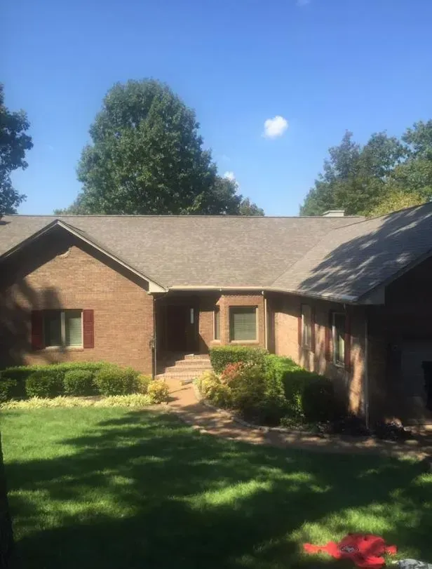 A brick house with a gray roof and a large lawn in front of it.