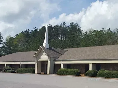 A church with a steeple and a parking lot in front of it.