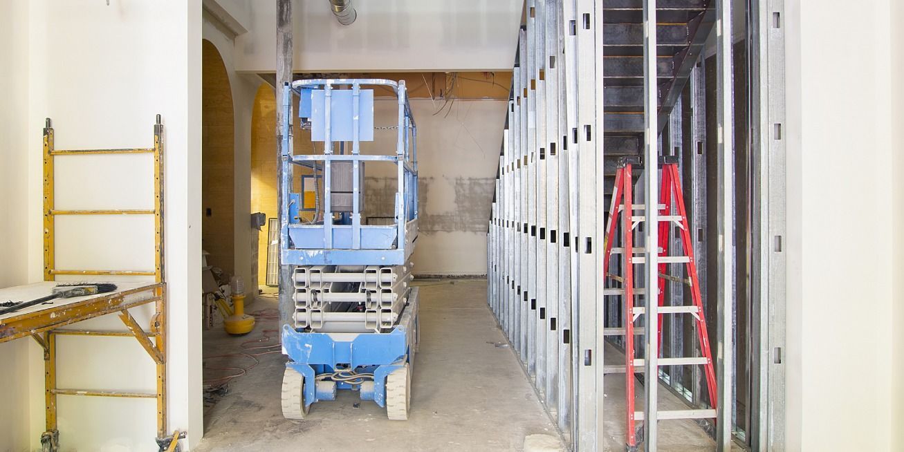 Construction site with a blue lift, red ladder, and metal wall framing.