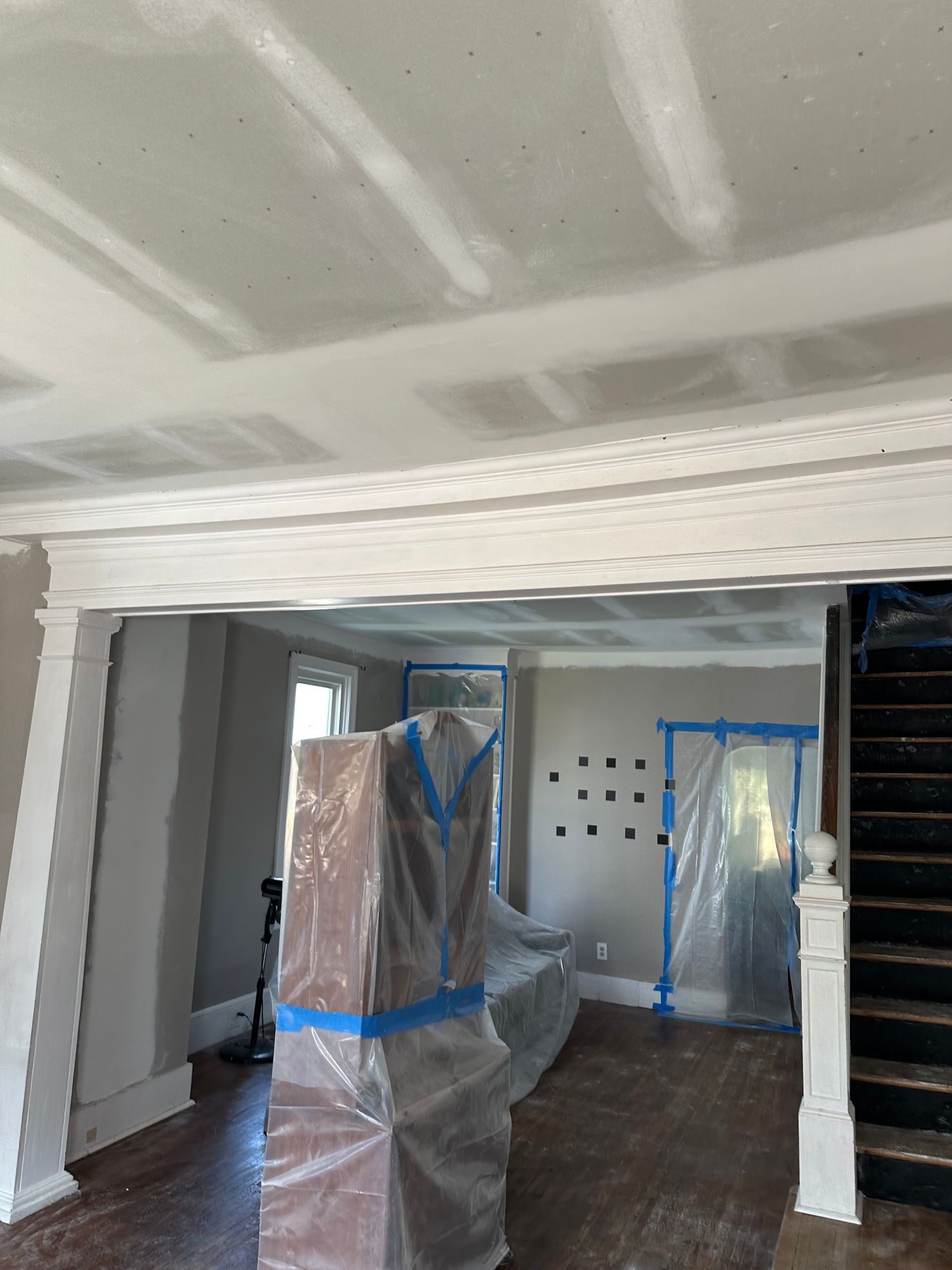 Room under renovation with exposed ceiling beams and trim, plastic covering furniture.