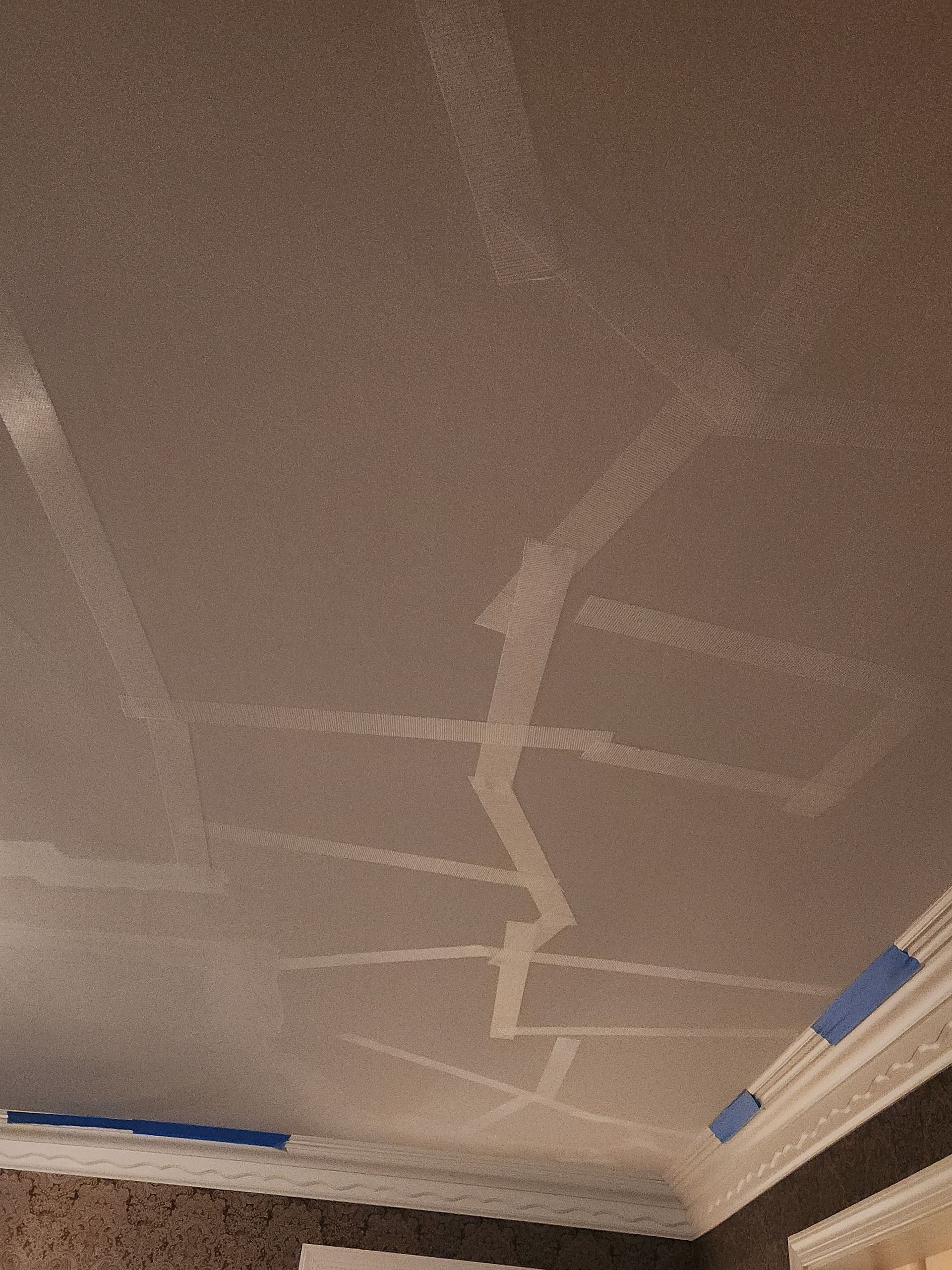 Cracked ceiling with white tape over the cracks. Blue tape is on the molding.