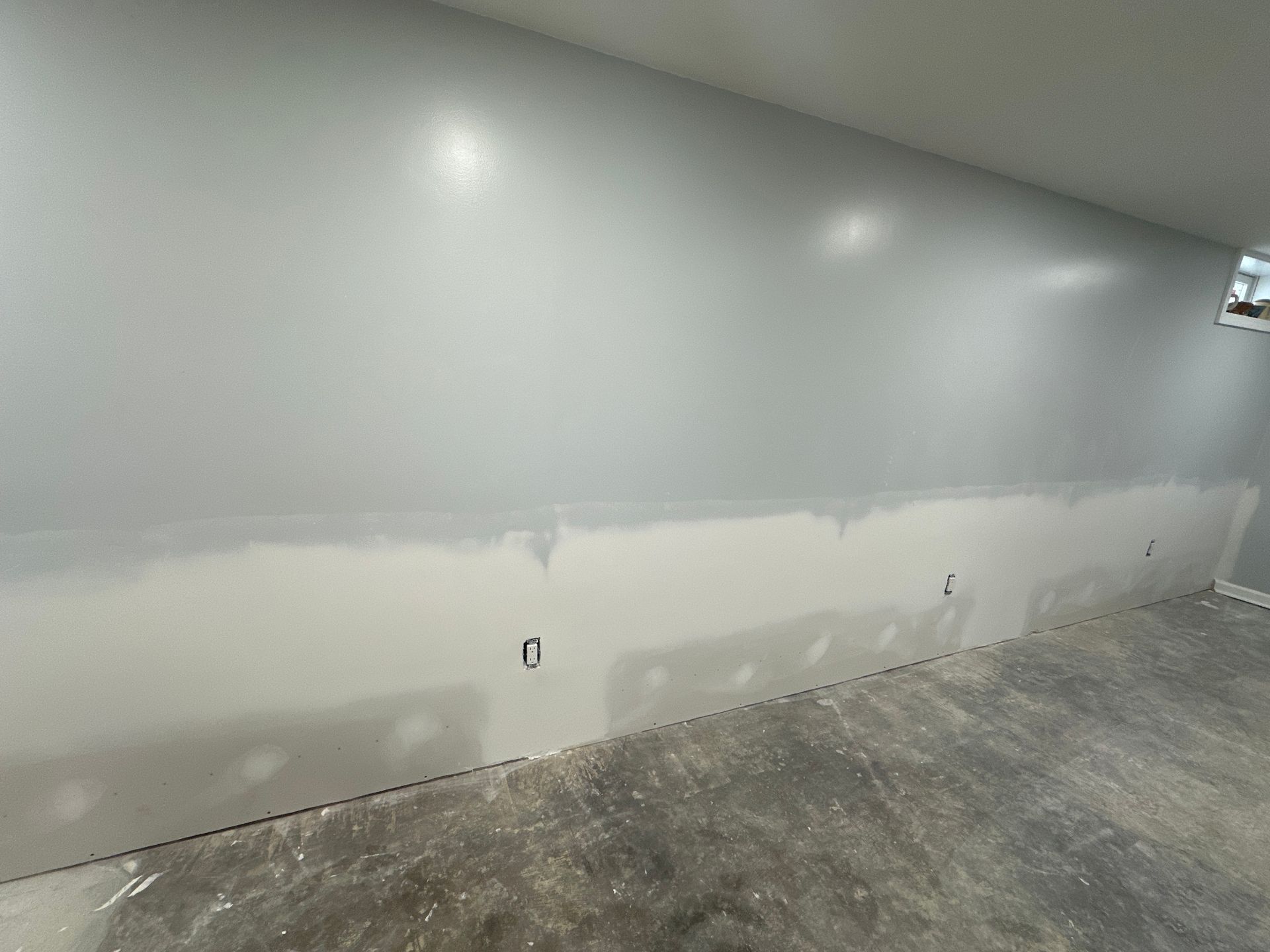 Wall, freshly painted light gray above a lighter strip, with electrical outlets. Concrete floor.