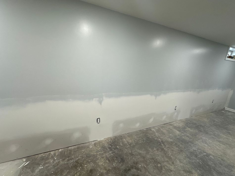 Wall, freshly painted light gray above a lighter strip, with electrical outlets. Concrete floor.