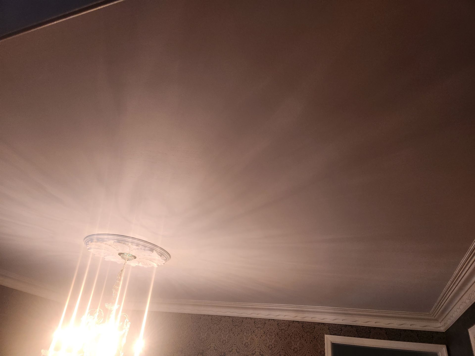 Ceiling with a glowing chandelier and crown molding.
