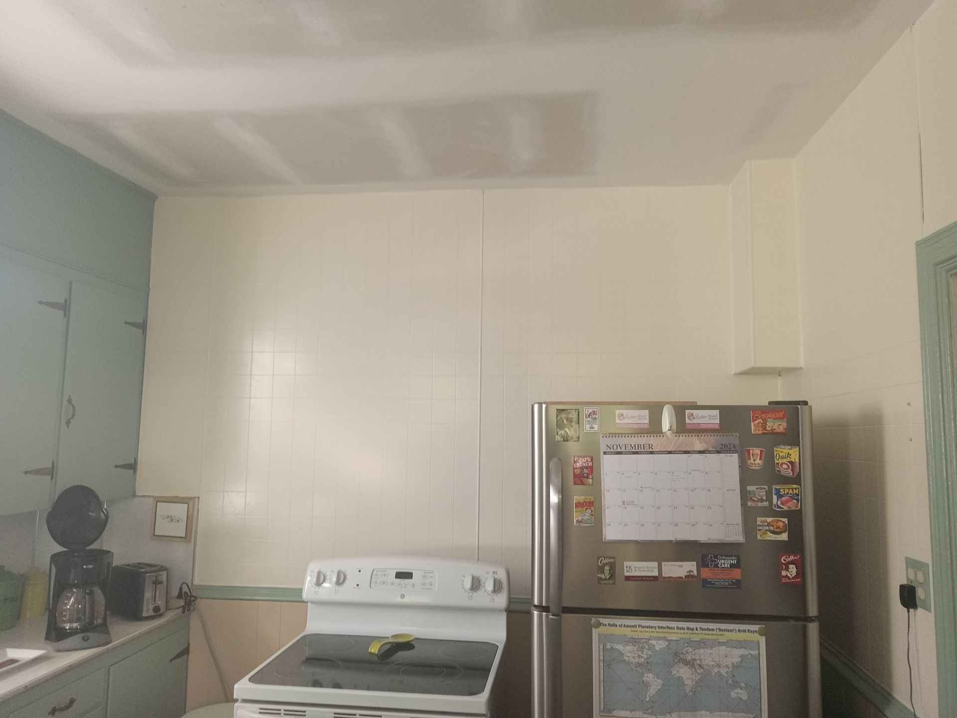 Kitchen with white walls, cabinets, and appliances: stove, refrigerator. Blue-green cabinet and door.