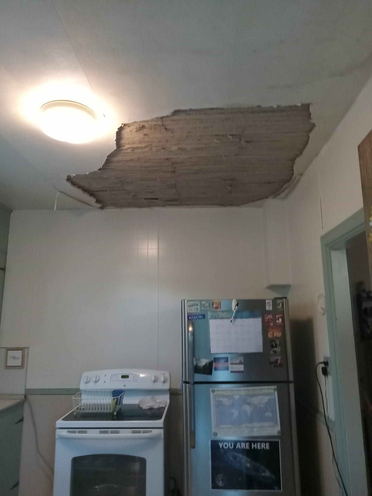 Kitchen ceiling with a large hole revealing the structural framework above, over a stove and refrigerator.