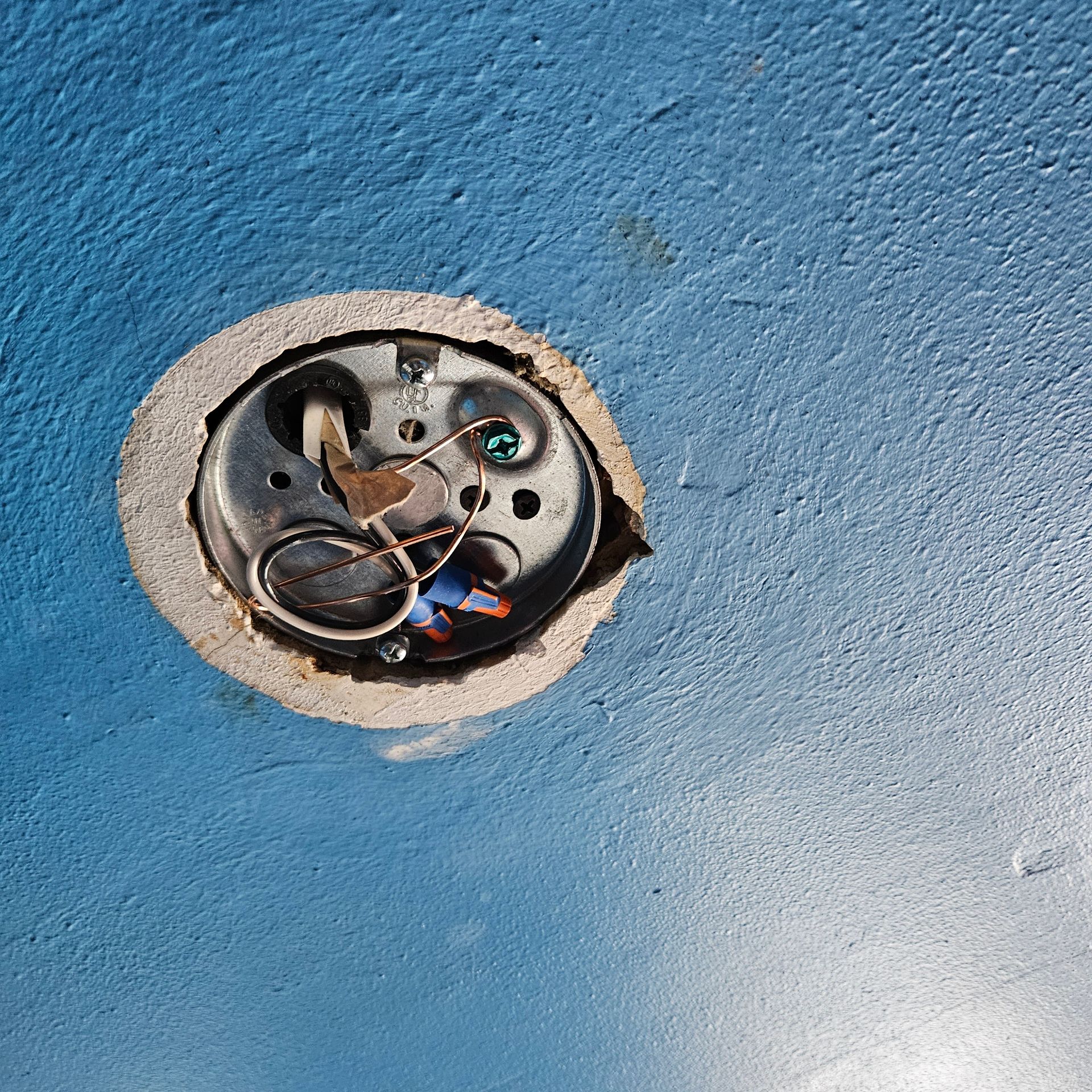 Open electrical fixture with exposed wires in a blue painted ceiling.