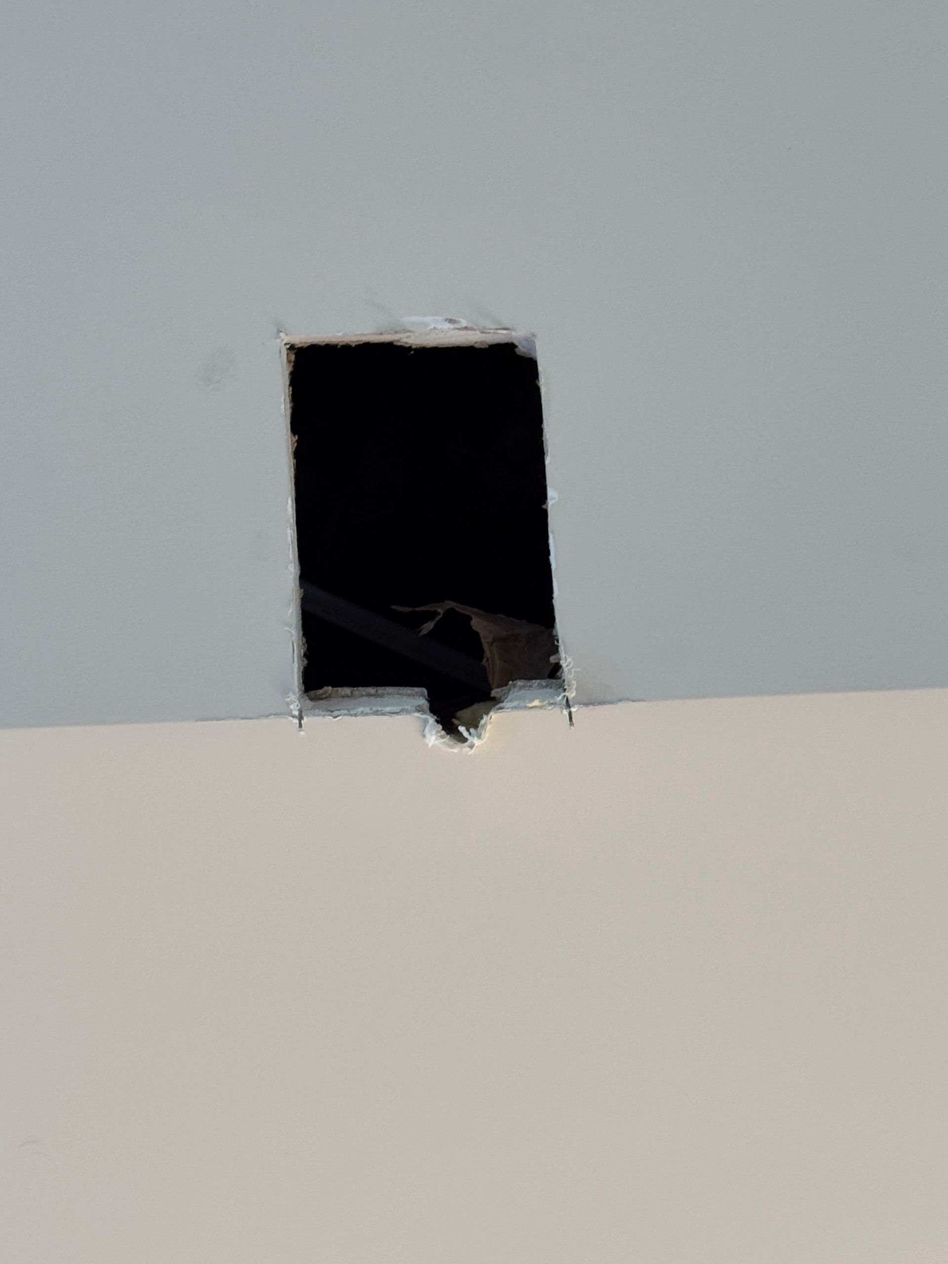 Hole cut in a white ceiling reveals a dark void with black wiring visible.