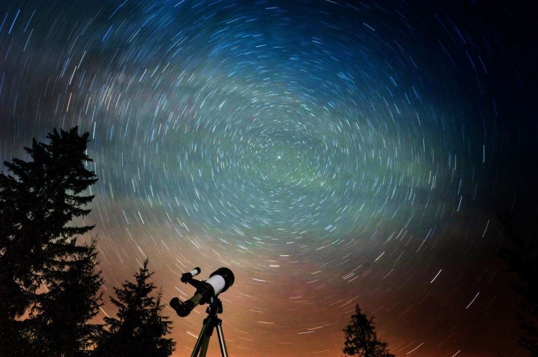 Silhouette of  a telescope under a swirling starry night sky with silhouetted trees