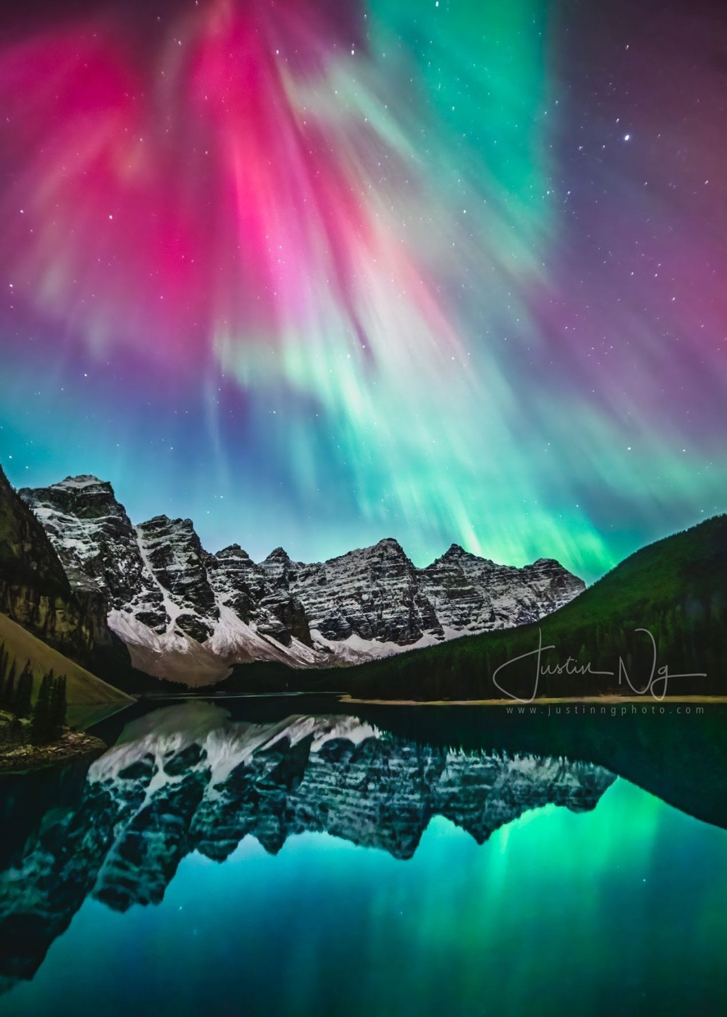Aurora lights over snow-capped mountains reflected in Moraine Lake at dusk