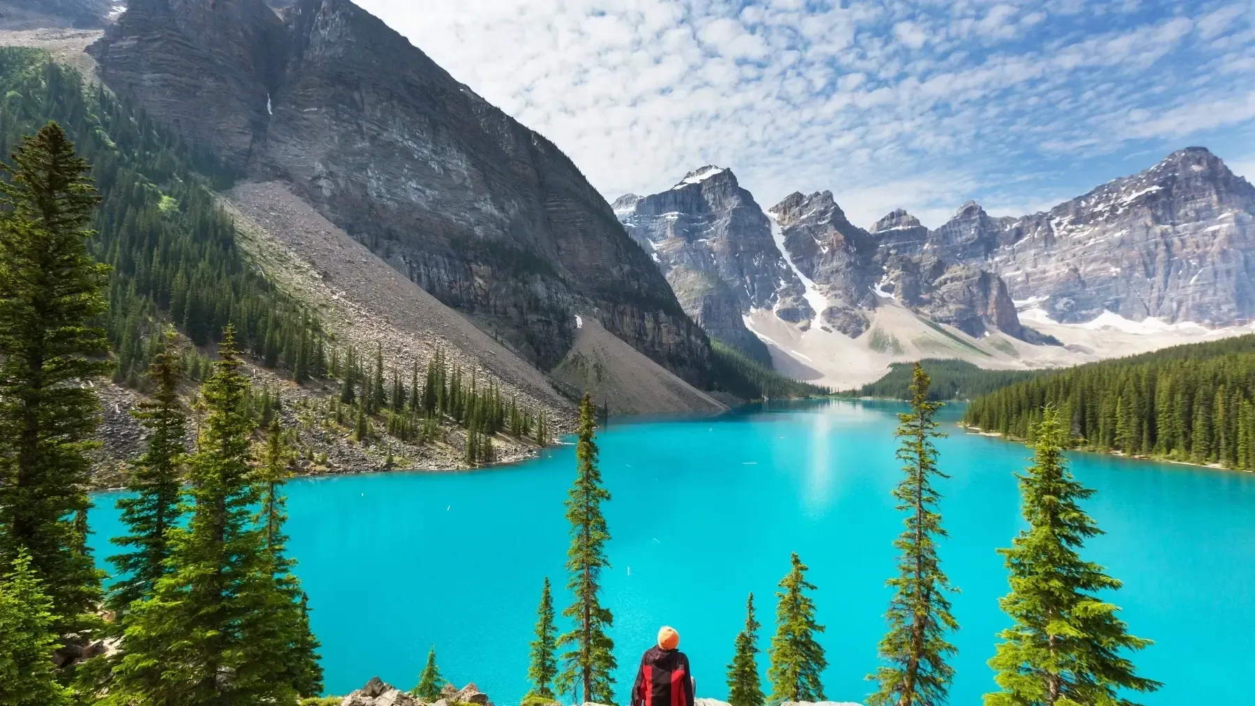Turquoise alpine lake reflecting forest, mountains, and sunlit peaks under a clear sky