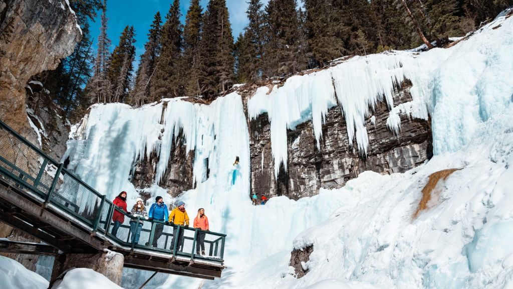 People on a viewing platform near a frozen waterfall and snowy cliff in a winter forest