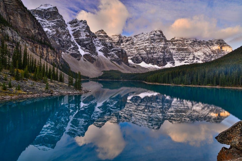 Snowy mountain peaks reflected in a calm turquoise lake under a cloudy sky.