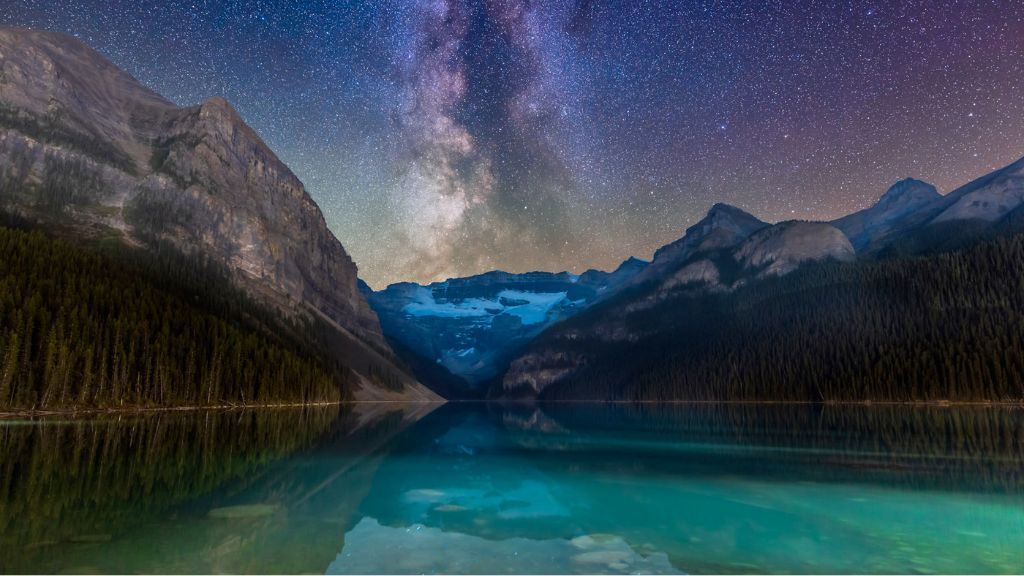 Starry night over a mountain lake with snow-dusted peaks reflected in calm water