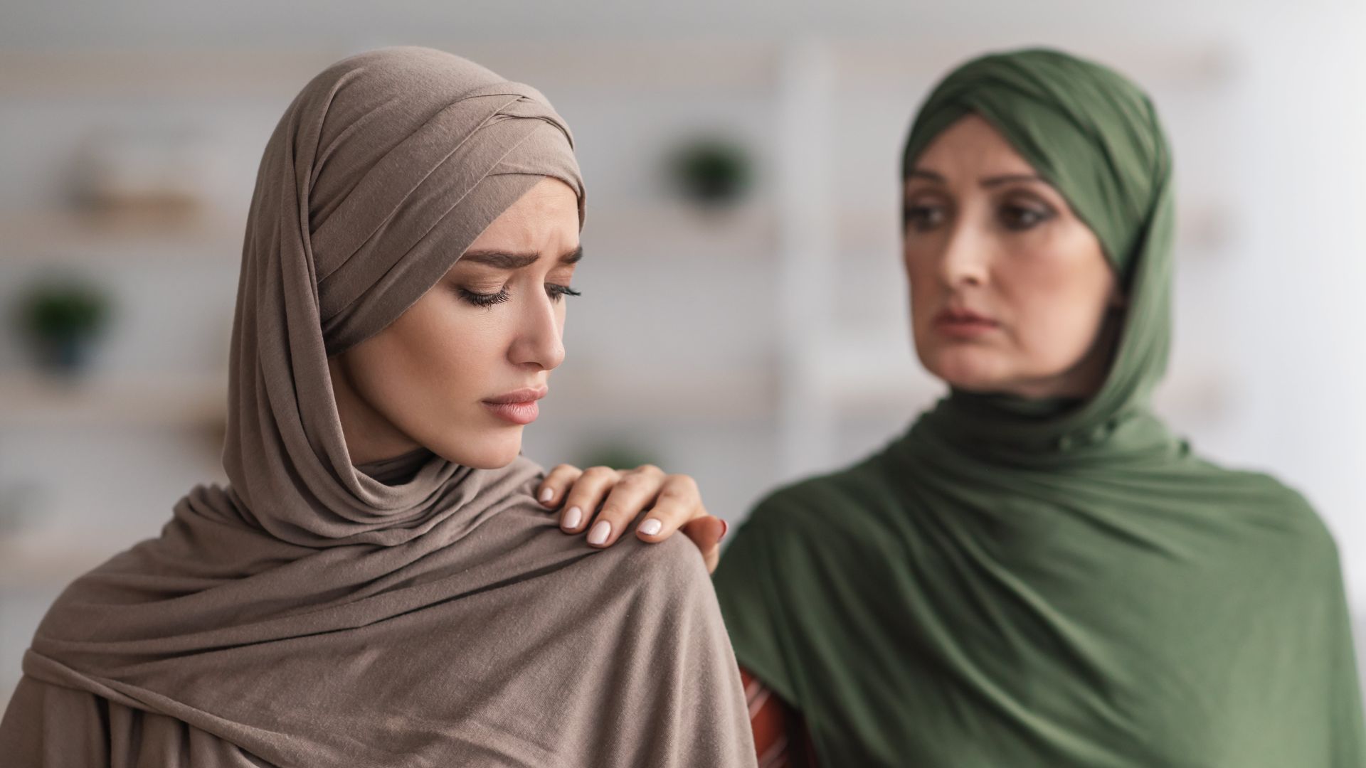 Woman in hijab comforted by another woman. The woman is touching the other woman's shoulder.