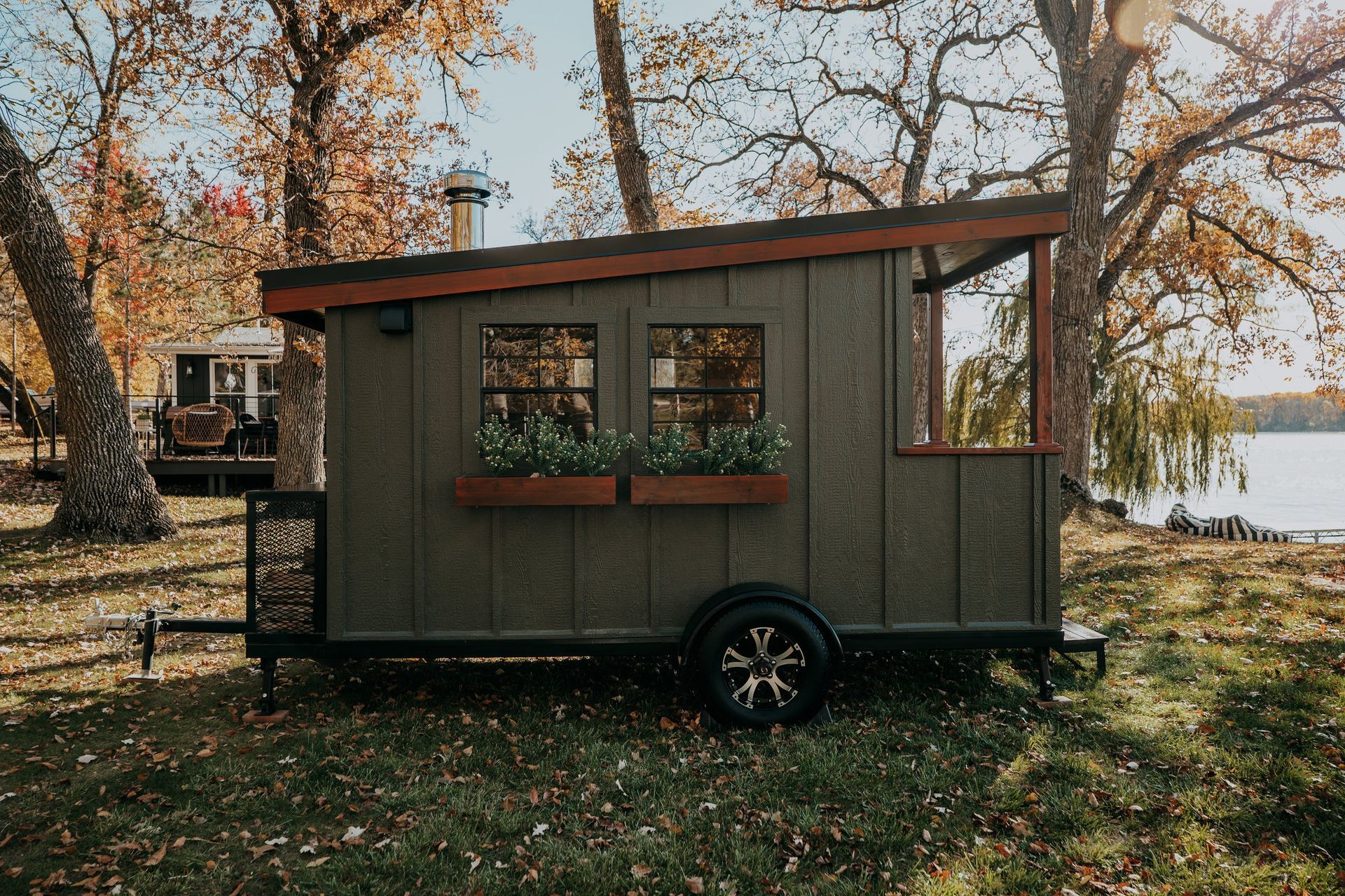 A tiny house on wheels is parked in the grass near a lake.