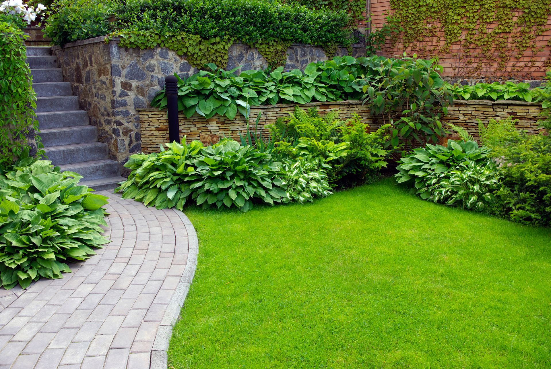 A brick walkway leading to a lush green lawn in a garden.