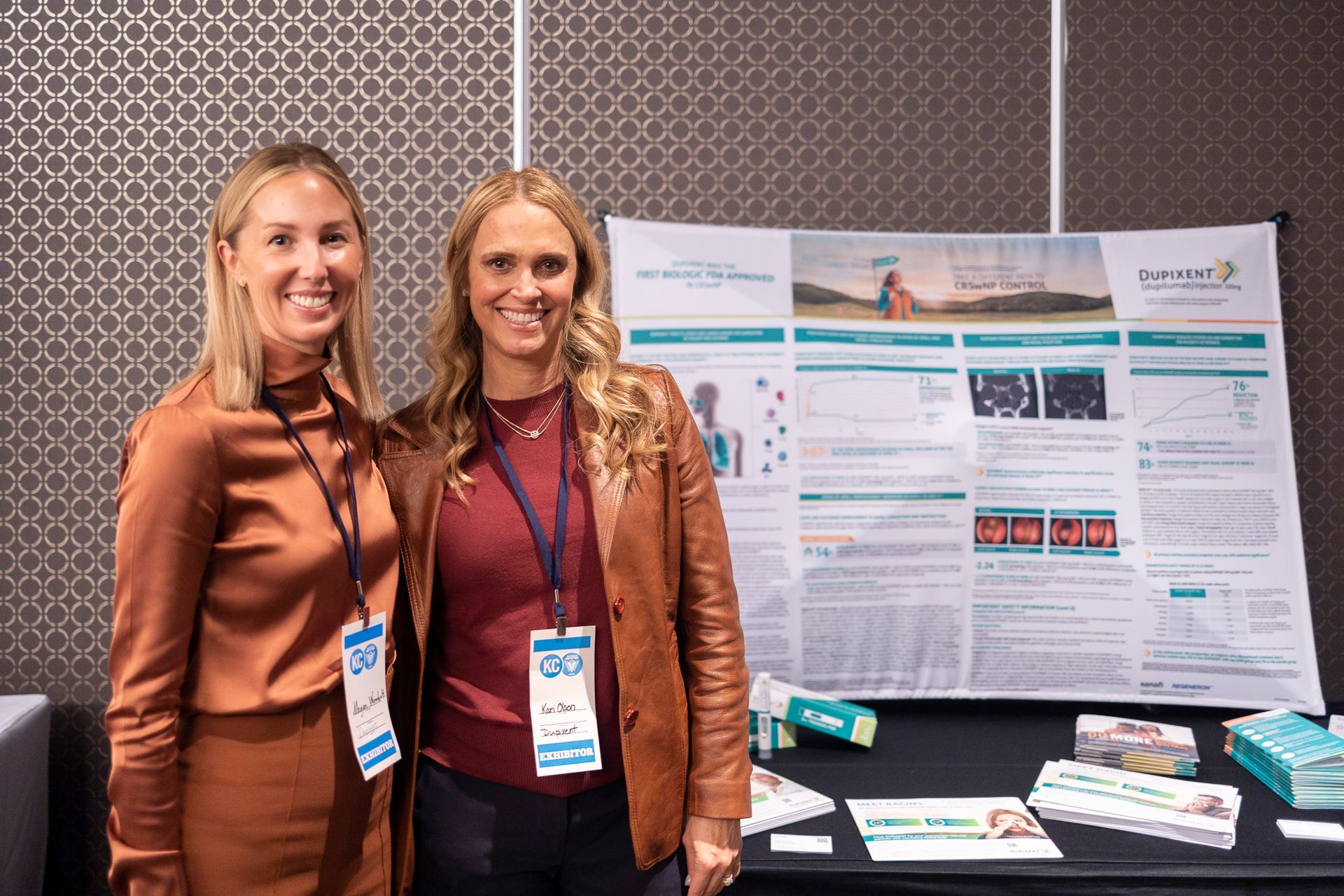 Two women are standing next to each other in front of a poster.