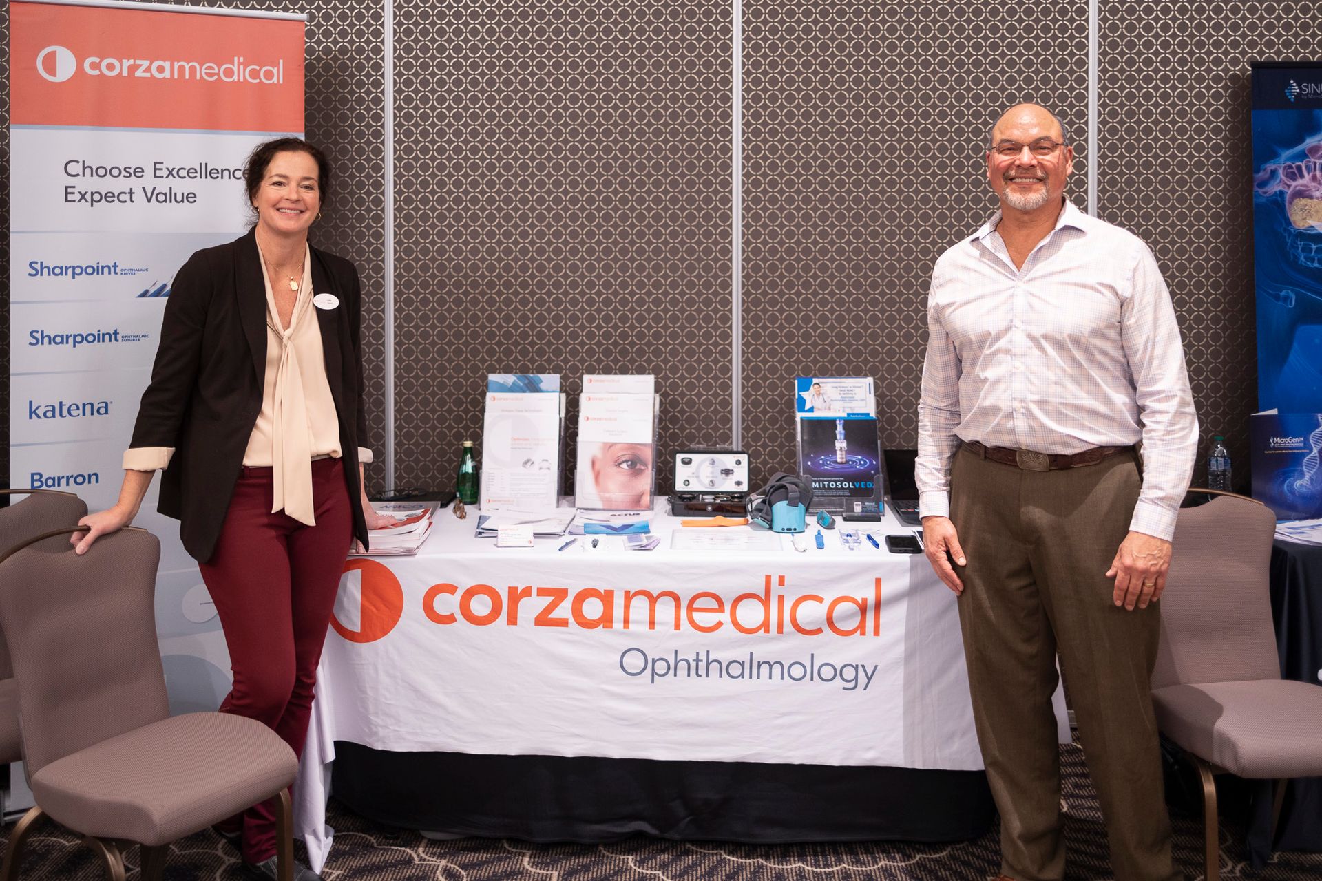 A man and a woman are standing in front of a table that says corzamedical ophthalmology