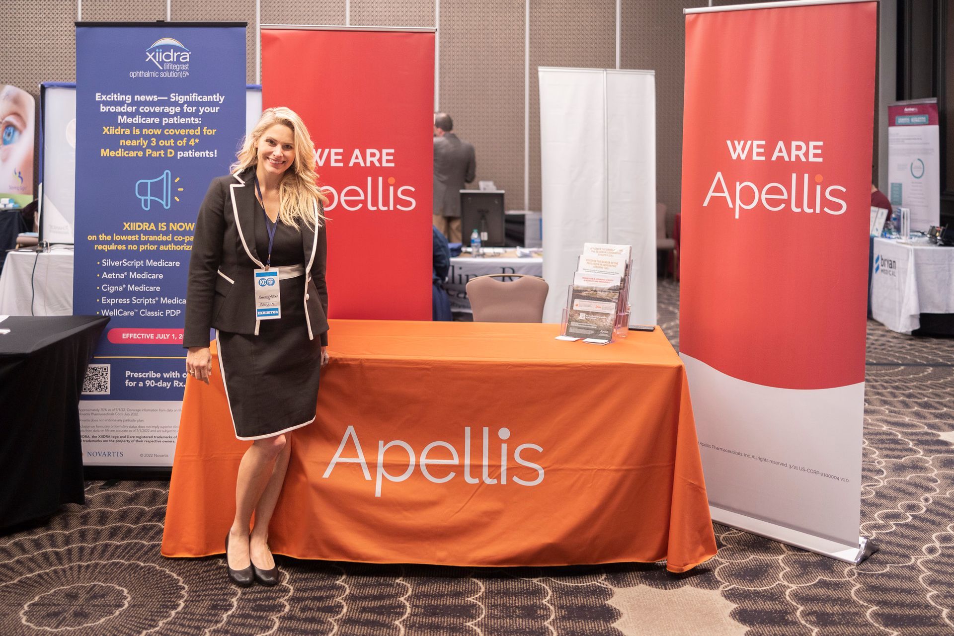 A woman is standing in front of a table that says we are apellis