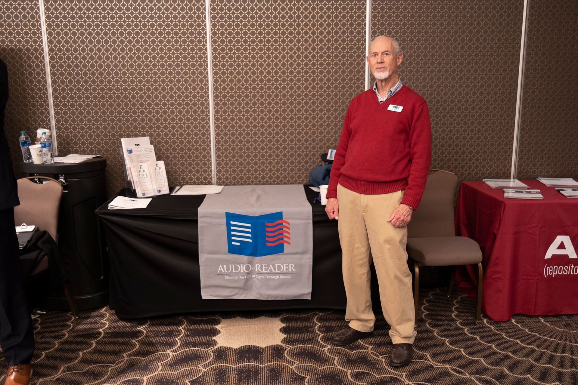 A man in a red sweater is standing in front of a table.