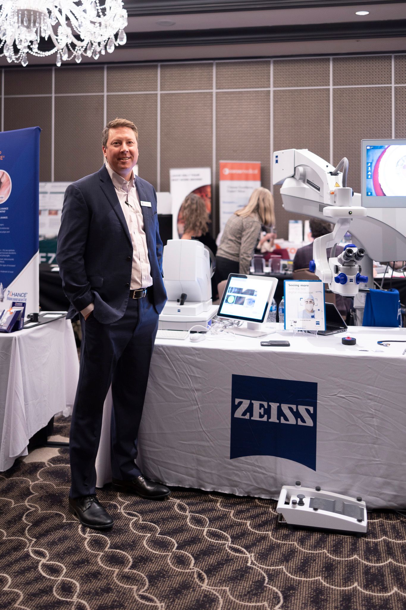 A man in a suit is standing in front of a table with a zeiss logo on it.