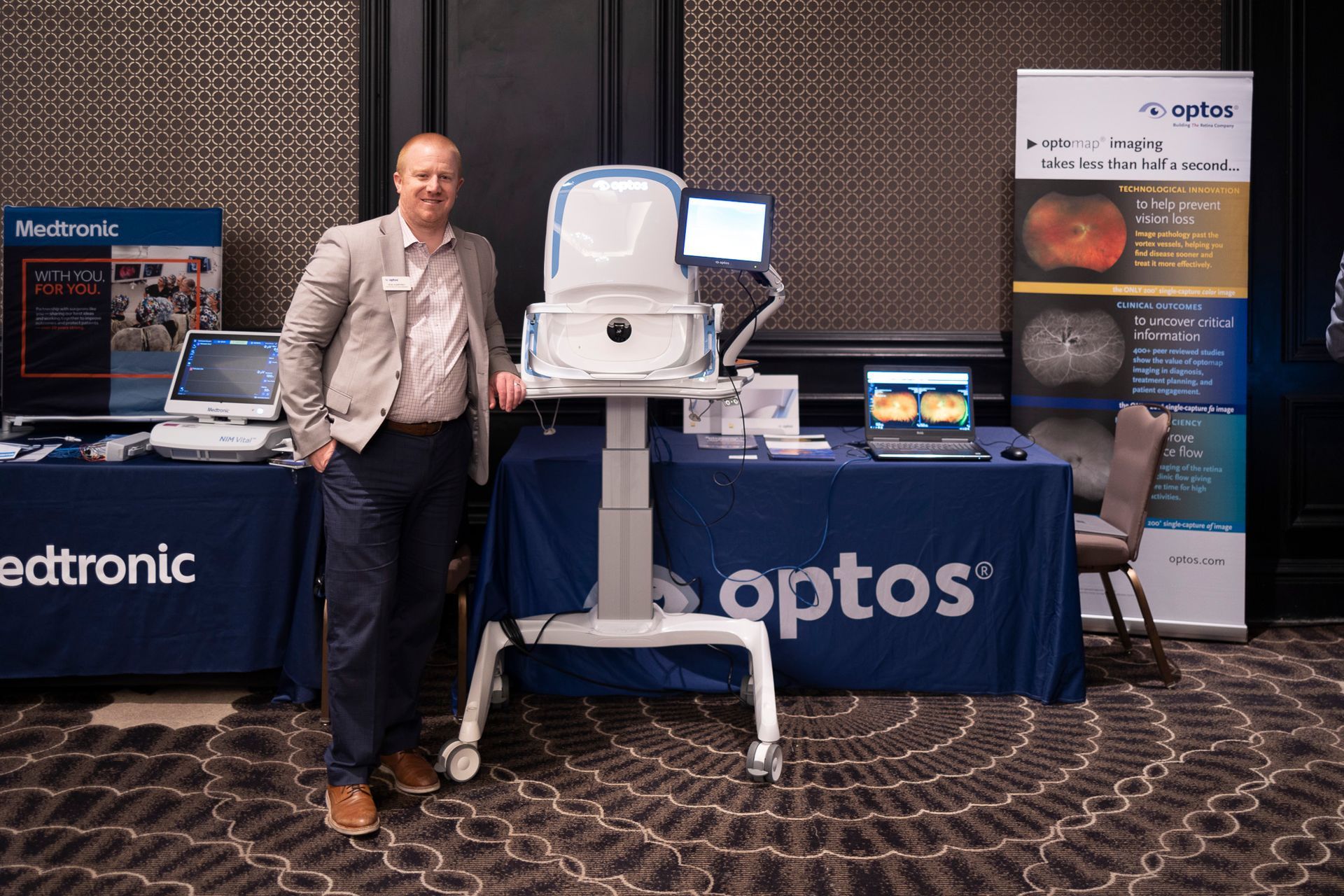 A man is standing in front of a table with a sign that says optos on it.